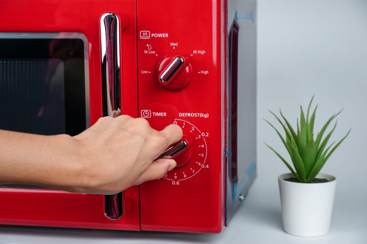 Woman's hand adjusting time with circle button to heat food from microwave in kitchen. Kitchen appliances using the concept.